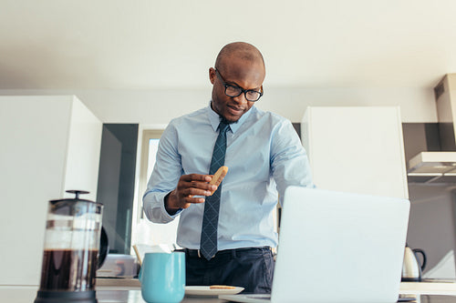 Businessman working on laptop computer while eating breakfast