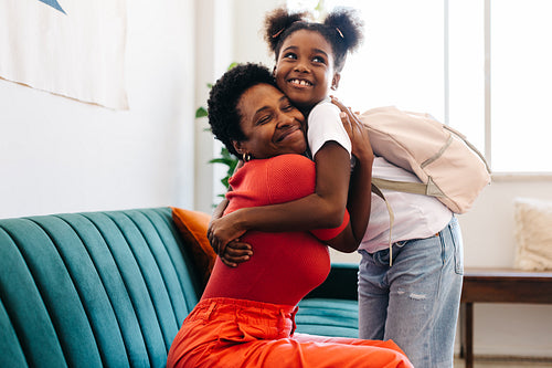 Happy mother and daughter hugging goodbye in living room for school morning routine