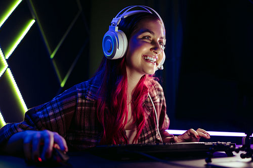 Happy female gamer smiling at her computer screen as she plays an online video game