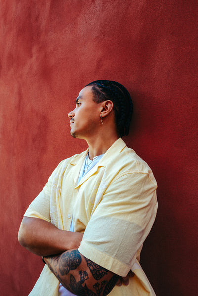Pensive latina man leans against a red wall outdoors in an urban portrait