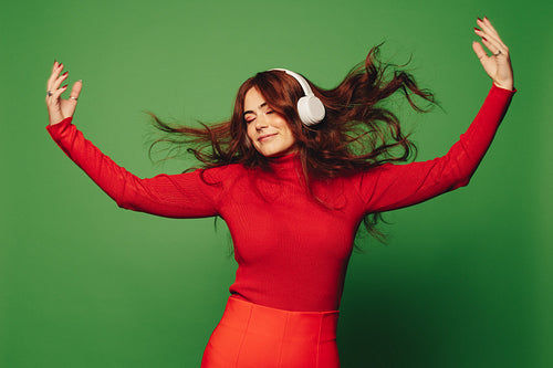 Happy woman dancing and celebrating with music headphones on a vibrant green background