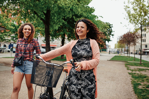 Smiling young friends with bicycle walking on city street