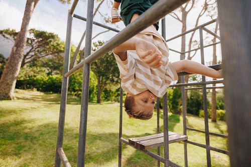 Boy hanging upside down on a jungle gym in a sunny park
