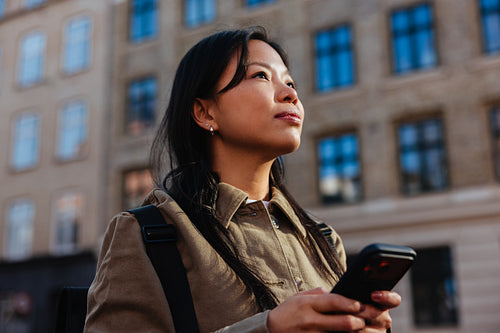 Woman with smartphone looks upward in city