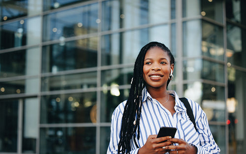Pensive business woman holding a smartphone and wearing earphones during her morning commute in the city