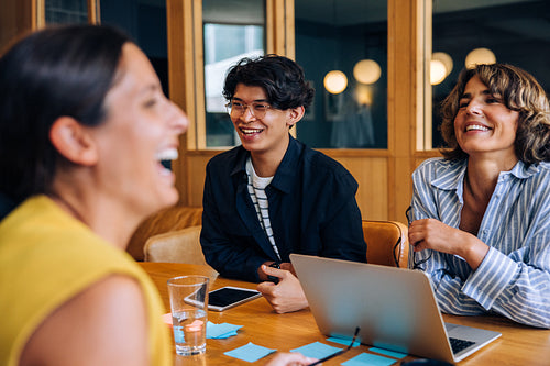 Three colleagues enjoying a lighthearted discussion around a table with laptops