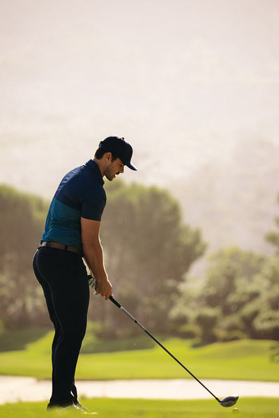 Sportsman aiming with driver, preparing to hit golf ball near sand bunker on serene golf course