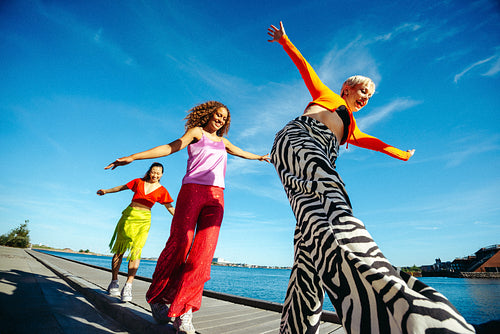 Friends walk and balance playfully on a waterfront boardwalk in sunny urban summer