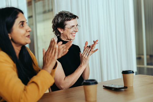 Two people clapping and smiling during an office meeting