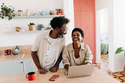 Mature black couple laughing and using a laptop in their home kitchen