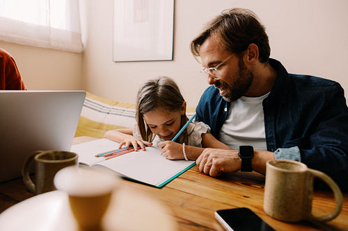 Father helps daughter with drawing at home
