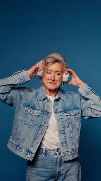 Happy senior woman with headphones enjoying music on blue studio background