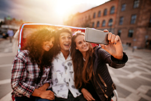 Three young friends taking selfie on tricycle ride.