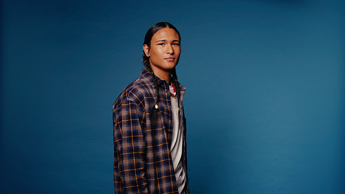 Young man with braids smiles for a portrait against a blue background