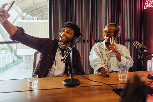 Podcast hosts enjoying live session, taking selfie, studio environment