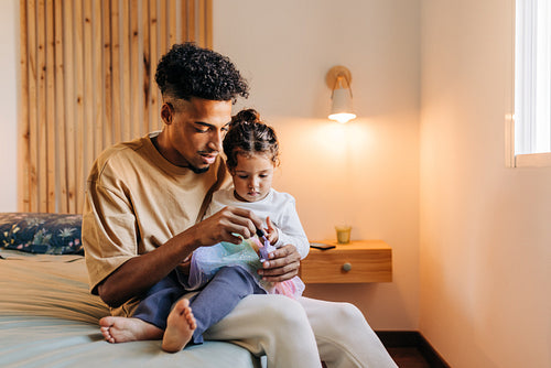 Young dad painting his daughter's nails with nail polish at home
