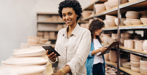 Cheerful female ceramist using a digital tablet in her shop