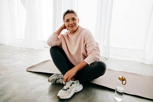 On a yoga mat, the woman rests with water after exercise at home