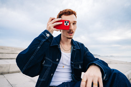 Young man taking photo with red phone outdoors