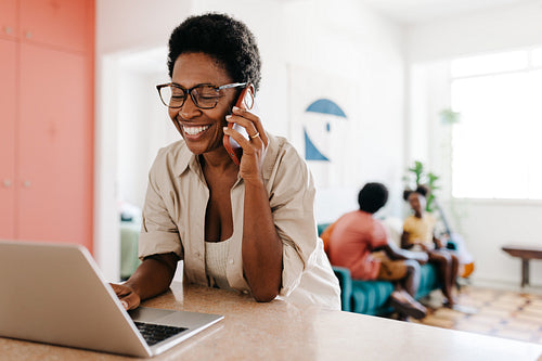 Happy working mom using a laptop while making a phone call at home