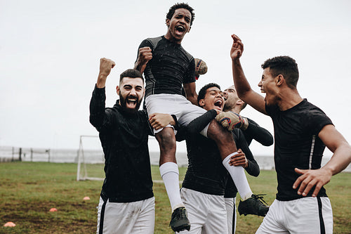 Soccer players celebrating success by lifting a teammate on shoulders