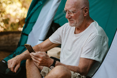 Senior man using phone at campsite