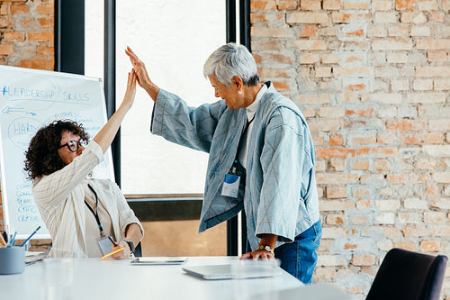 Two colleagues exchanging a high-five in celebration during a successful team meeting in an office with a brick wall background