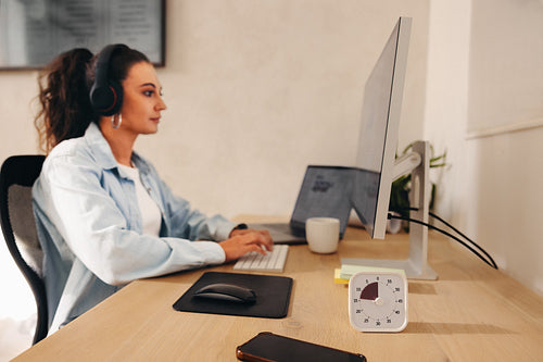 Focused woman working at desk with timer and computer in an office