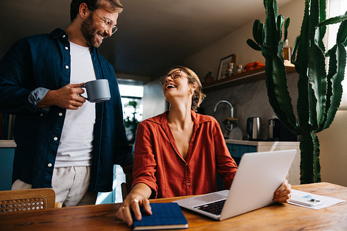 Happy couple laughing together with laptop and coffee at home
