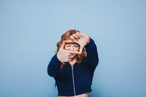 Young woman making a finger frame while standing in a studio