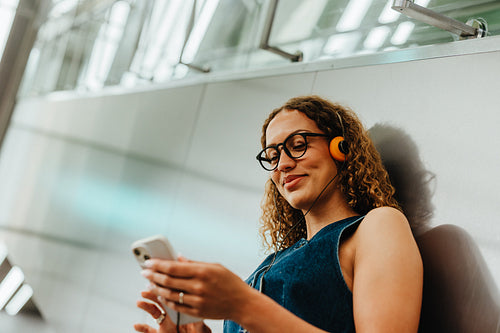 Woman using smartphone with headphones in urban train station