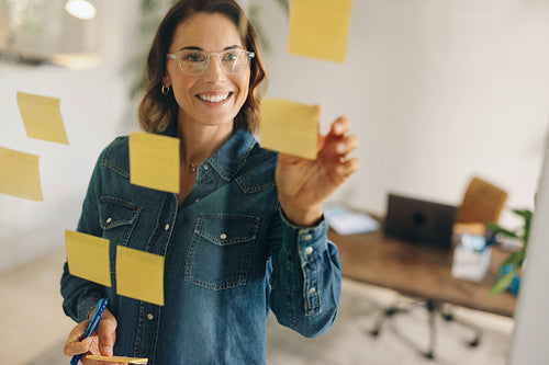 Creative businesswoman brainstorming ideas in glass-walled office