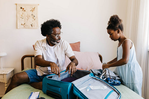 Father guiding his daughter in packing travel essentials for a family vacation