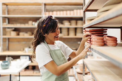 Happy young craftswoman looking at her handmade ceramic products in her shop