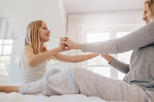Little girl playing with her mother on bed.