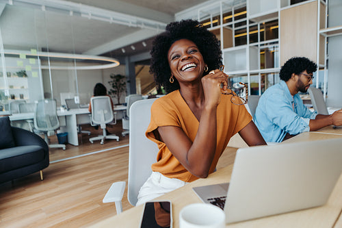 Happy businesswoman sitting in a startup office and working on a laptop