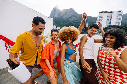 Brazilian friends dancing funk and celebrating with drinks on a rooftop in Rio