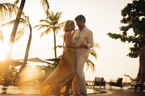 Elegant couple dancing poolside at sunset