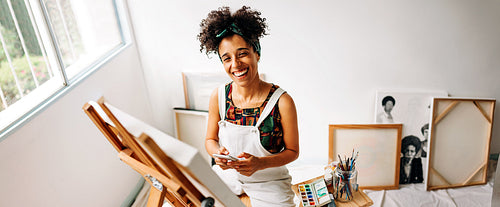 Cheerful painter holding a smartphone in her art studio