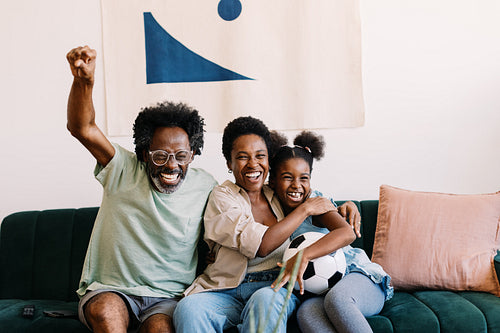 Parents and their daughter enjoy watching a football game on tv