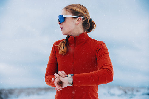Winter running pauses as a runner checks her watch in falling snow