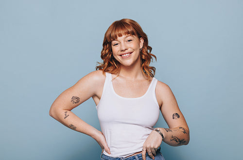 Carefree young woman with tattoos smiling at the camera while standing in a studio