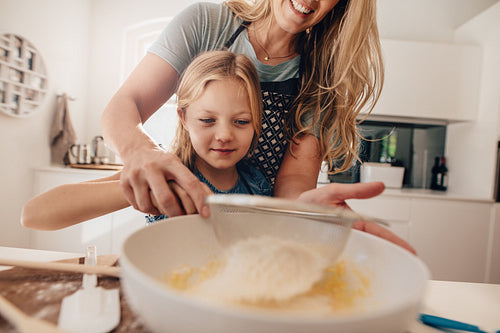 Little girl learning to make batter from her mother