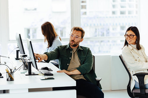 Male software designer sitting at his desk and talking to his colleague