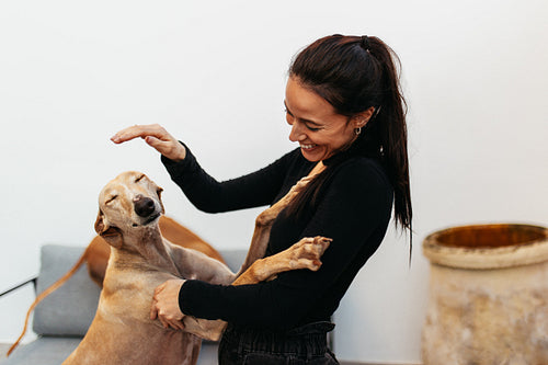 Happy young woman petting her dog at home