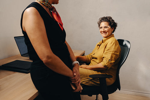 Casual discussion between two businesswomen at an office desk during work