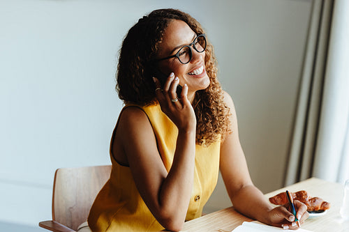 Smiling woman talks on phone in a cafe with notebook and coffee