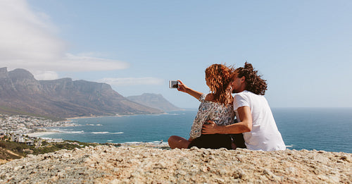 Couple sitting on the top of mountain and taking selfie