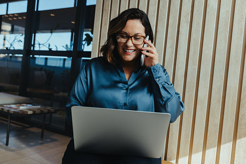 Business woman using laptop and phone in a modern office workspace