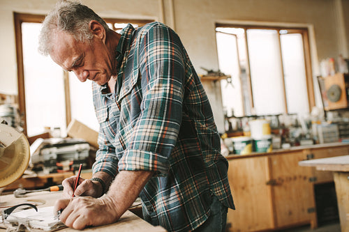 Skilled male carpenter making drawings on clipboard